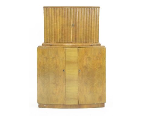 An Art Deco 'Miramar' walnut cocktail cabinet,with a bow front, the upper section with a fluted cupboard, the interior with a