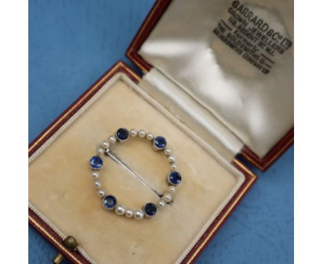 A sapphire and pearl brooch, of circular form set in white metal marked 9ct, approximately 3.5 grams in a Garrard &amp; Co Lt