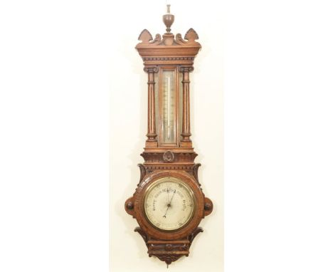 A late Victorian oak cased wall barometerThe centered silvered dial with glazed mercury thermometer, housed within twin Corin