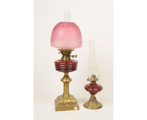 Two early 20th Century oil lampsThe first rising from a brass base with ribbed cranberry glass oil receptacle and etched foli