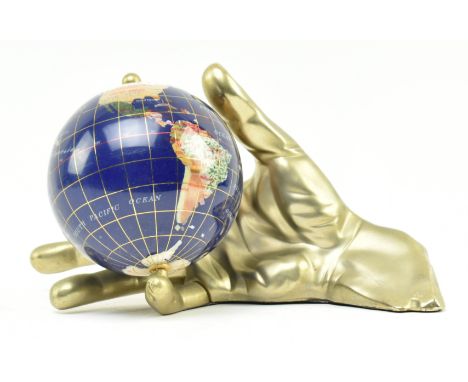 A vintage Hollywood Regency style semiprecious stone inlaid rotating globe, cast within a brass oversized hand. The globe wit