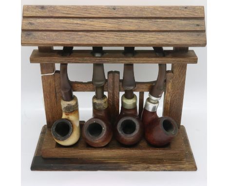 Three Peterson pipes, two with Irish silver collars, and a Plumb example, in an oak pipe rack. UK P&amp;P Group 2 (£20+VAT fo