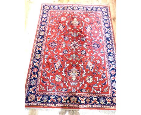 A red ground Indian woollen red ground carpet embroided with stylised flowers within a blue frieze border 207x139cm