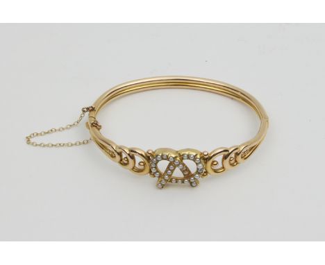 A Victorian 15ct gold and half pearl hinged bangle, the front of openwork 'lovers knot' motif set with pearls, marked 15ct on