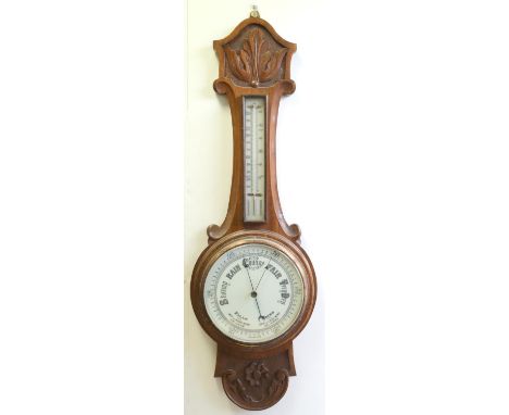 WHEEL BAROMETER WITH A CIRCULAR WHITE ENAMELLED DIAL ENCLOSING AN ANEROID MOVEMENT, WITH A THERMOMETER ABOVE, IN A CARVED OAK