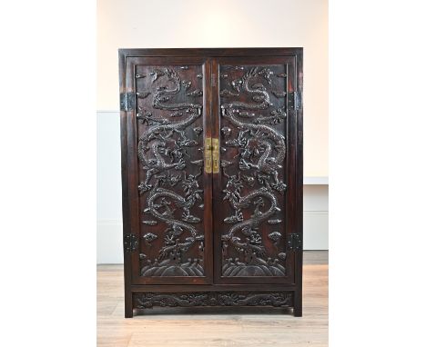 A CHINESE CARVED HARDWOOD CABINET, 20TH CENTURY. Of rectangular form with carved dragon doors. Single shelf to the interior a