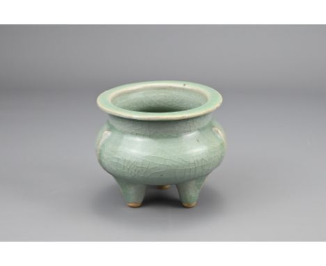 A CHINESE CELADON GLAZED TRIPOD CENSER. Compressed body with three narrow flanges vertical from the shoulder on three conical