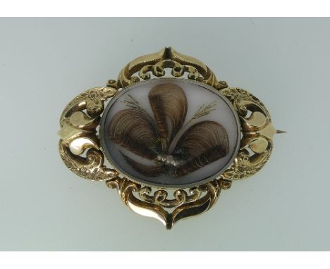 A Momento-Mori Brooch, in unmarked yellow metal, with elaborate pierced and engraved frame, the centre with a fine hair and s
