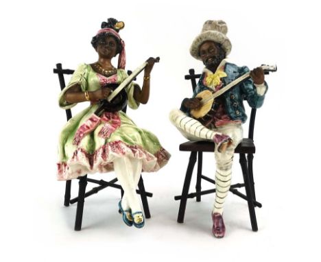 A pair of Goldscheider-style majolica figures modelled as a male musician and his female companion, each seated on a faux bam