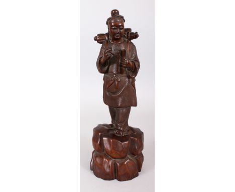 A 20TH CENTURY CHINESE CARVED WOOD FIGURE OF A YOUTH STANDING ON A ROCKY PLINTH, holding in his hands a scroll and a pen, 12.