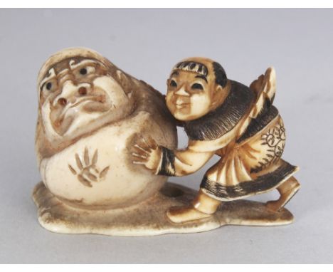 A SIGNED JAPANESE MEIJI PERIOD IVORY NETSUKE OF A BOY & A DARUMA DOLL, the large doll being pushed by the boy on a shaped bas