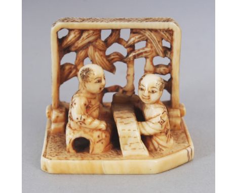 A JAPANESE MEIJI PERIOD IVORY NETSUKE OF TWO BOYS, reading an open scroll in front of a pierced screen, 1.25in wide & 1in hig