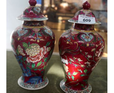 A late 19th/early 20th Century French enamel painted lustre form lidded vase decorated upon a cranberry red ground (2)