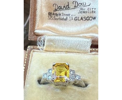 An Art Deco style yellow sapphire and diamond ring, the emerald cut yellow sapphire with-in white metal claw set mount with s