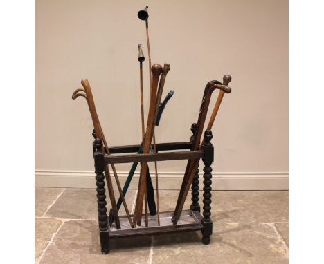 A collection of walking sticks and canes to an early 20th century bobbin turned oak stick stand, to include; two brass church