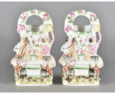 A pair of 19th Century Staffordshire watch holders, in the form of a seated Highland couple, she with tambourine, he with lut