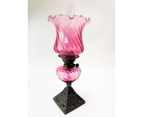 A Victorian cast iron and cranberry glass oil lamp. The base cast with dragons, with a wrythen cranberry glass shade, height 
