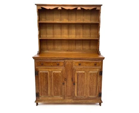 An Arts and Crafts light oak dresser in two parts. The top with carved frieze and two grooved shelves above a base with two s