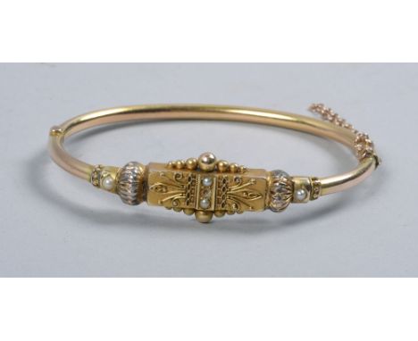 An Edwardian gold bangle with a beaded plaque, line filigree and seed pearl set.