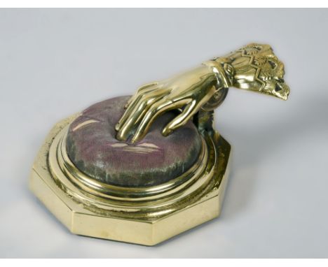 A Victorian octagonal brass needlework cushion material clamp  formed by a sprung hand securing the material on the pin cushi