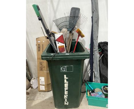 A WHEELIE BIN CONTAINING A LARGE QUANTITY OF GARDEN TOOLS TO INCLUDE RAKES AND A LIGHT BOARD ETC 