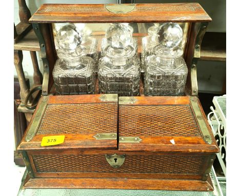 An Oak cased decanter set with three cut glass decanters, mirror back with woven effect double hinged from, brass bindings 