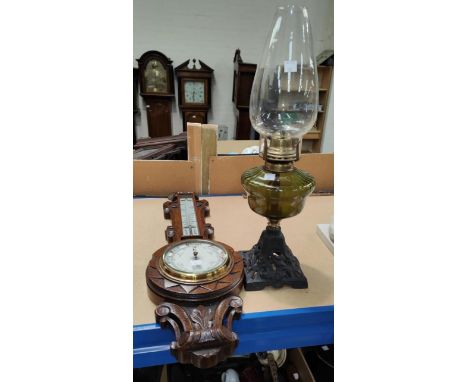 An Edwardian barometer with thermometer in carved oak case; a cast iron and glass oil lamp 