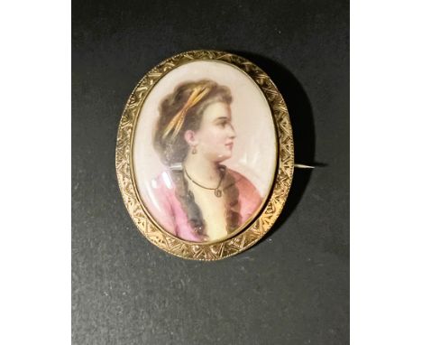 A miniature bust portrait on porcelain brooch of a young lady in 18th century dress in yellow metal surround 