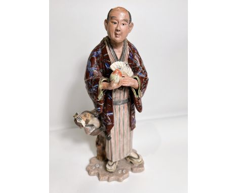 A late 19th/ early 20th century ceramic figure of a man with fan and monkey hanging from his Haori in a jacket of his own, wi