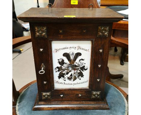An oak hanging cupboard with studded decoration with metal mounts and central milk glass panel with painted crest decoration 