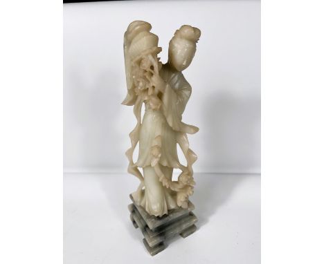 A light jade coloured soapstone figure Guan Jin holding up a basket of flowers on grey mottled plinth height 30cm 
