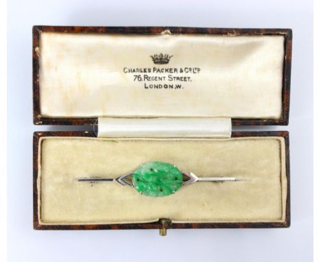 An Art Deco jade brooch, the central oval carved panel depicting fruit and foliage, set in a white metal stylised bar brooch,
