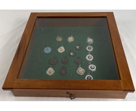 A glass topped small table top display cabinet containing a collection of vintage sports medals. To include football and netb