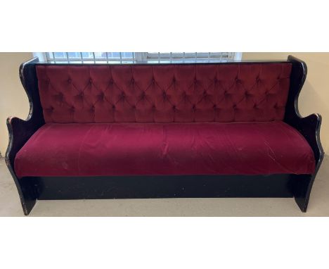 A vintage painted black wooden pub bench seat with button back red velour upholstery and shaped sides. Obtained from a local 