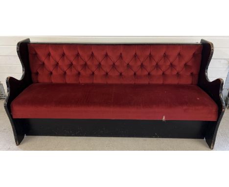 A vintage wooden bench seat painted black with button backed red velour upholstery and shaped ends. Obtained from a local pub