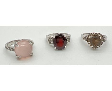 3 silver stone set dress rings All by The Genuine Gem Company. A central oval cut garnet with small round cut clear stones to