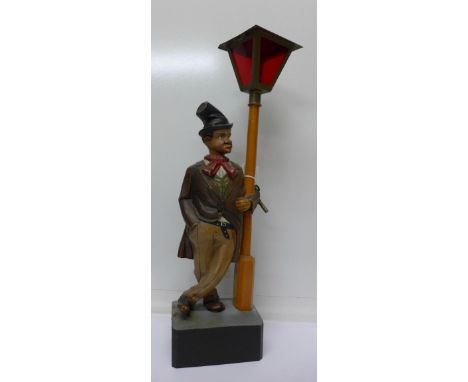 A Black Forest carved figure of a whistling tramp leaning against a lamppost, moving head, clockwork movement, with key (lamp