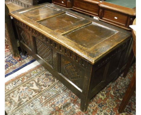 An 18th Century oak coffer, the plain three panel top over a dentil frieze and central dragon scale carved panel flanked by t