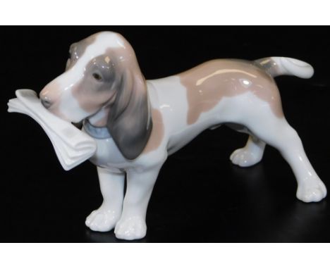A Lladro figure of a Bassett hound, with newspaper to the mouth, printed marks beneath, 19cm W. 