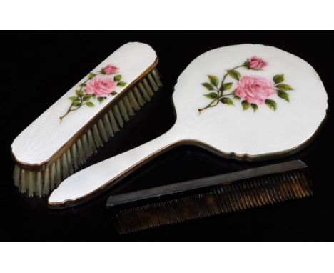 A silver backed comb, London 1961 and an enamel backed hand mirror and matching clothes brush, both with rose bud decoration.