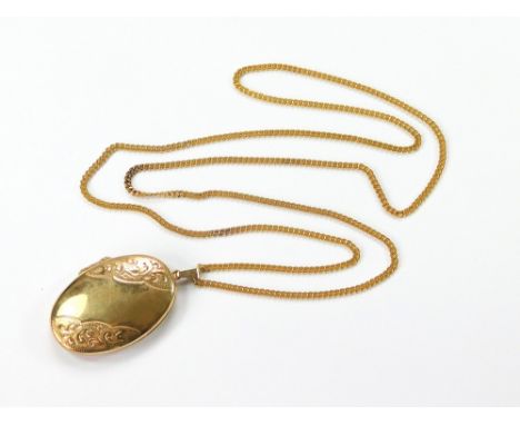 GOLD LOCKET. A 9ct. gold, oval, engraved locket. Length including bale, 4.7cm. Hung on a flat, curb link, gold-plated chain, 