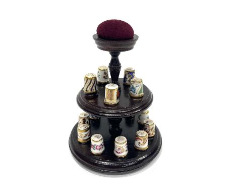 A collection of fifteen Royal Crown Derby thimbles on two tier turned wooden stand with pin cushion finial (16)