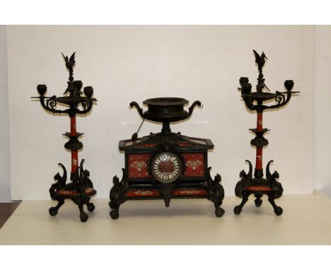 An unusual red enamel mounted spelter clock garniture, of neo-classical design, comprising a pair of three light candelabra w