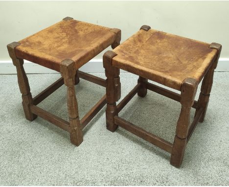 Robert "Mouseman" Thompson, pair of oak stools, each with rectangular hide top on faceted turned supports with understretcher