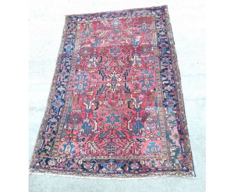 Persian Heriz carpet with stylised flowers and foliage in a red field surrounded by an indigo border and guard stripes, appro