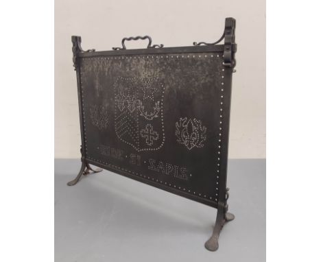 Dark metal firescreen with carrying handle and pierced panel with a coat of arms, on cheval supports.