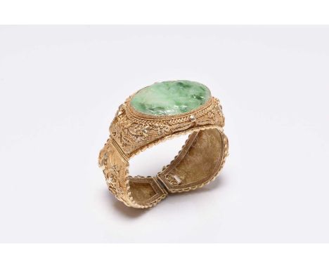 A jade and gilt metal bangle, designed as a central carved jade plaque depicting a bird amongst fruit, set to decorative fili