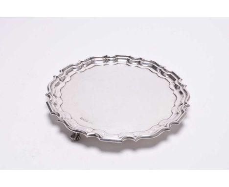 A silver card waiter, Walker &amp; Hall, Sheffield 1929, of circular form with pie crust rim and raised on three scroll feet,