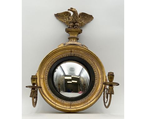 A Regency giltwood and ebonised convex girandole with a pair of scrolling gilt metal candle sconces, and surmounted by a carv