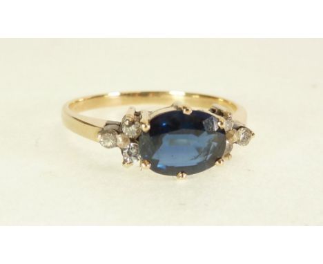 STAMPED 18CT GOLD SAPPHIRE AND DIAMOND RING, six claw horizontally set oval cut sapphire, flanked either side by an arrangeme